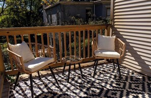 Eine Holzterrasse mit zwei Korbstühlen und einem kleinen runden Tisch.