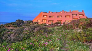 A large, multi-story building with a unique architectural design, situated on a hillside with a view of the ocean. - Casa Audrey by Wonderful Italy (Santa Teresa di Gallura)