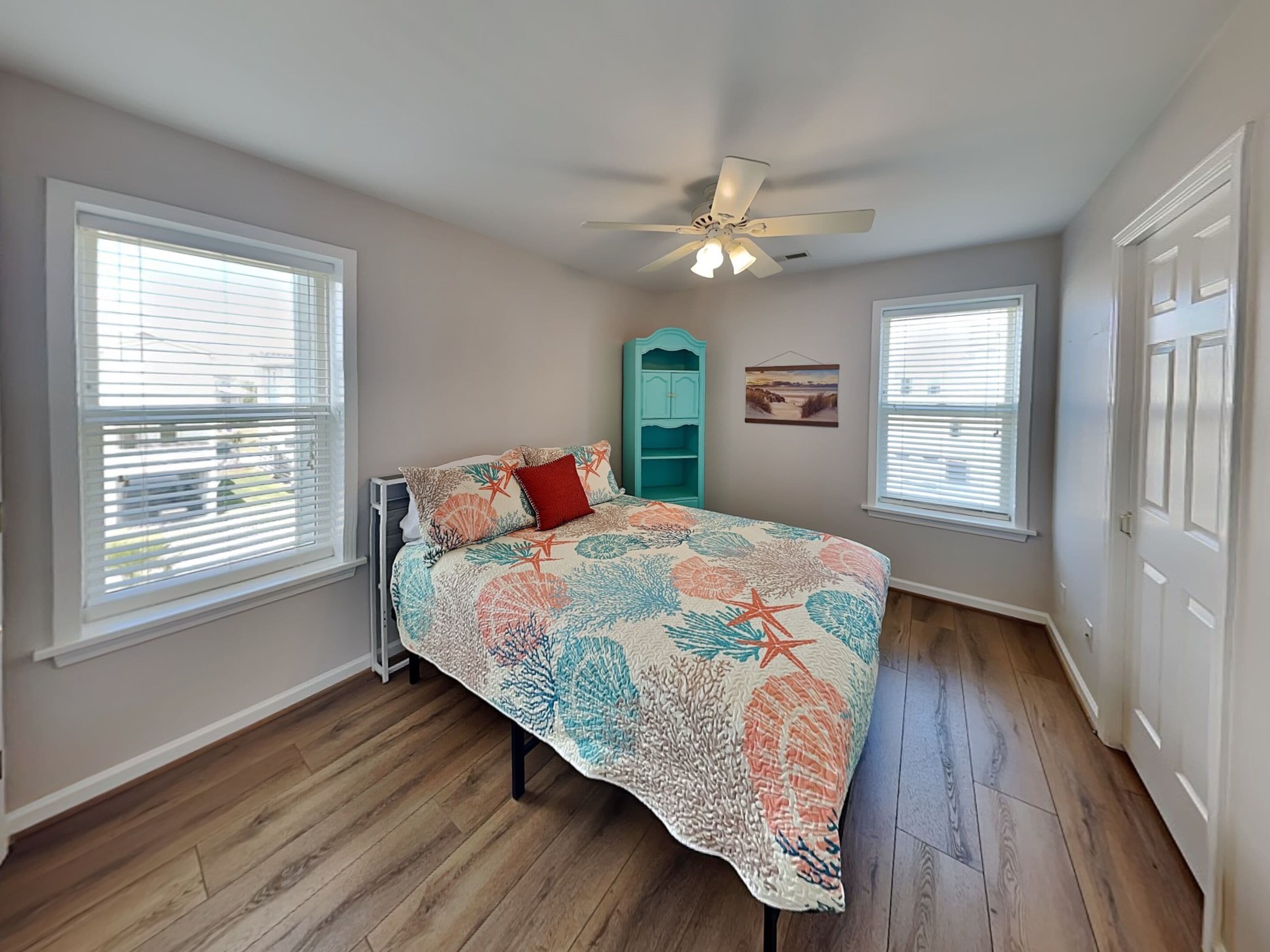 A bedroom with a bed, a ceiling fan, and two windows.