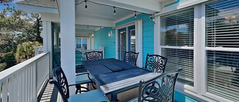 A covered outdoor patio with a table and chairs, a railing, and a view of the surrounding area.
