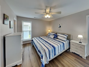A bedroom with a bed, a ceiling fan, a nightstand, a dresser, and a window with blinds.