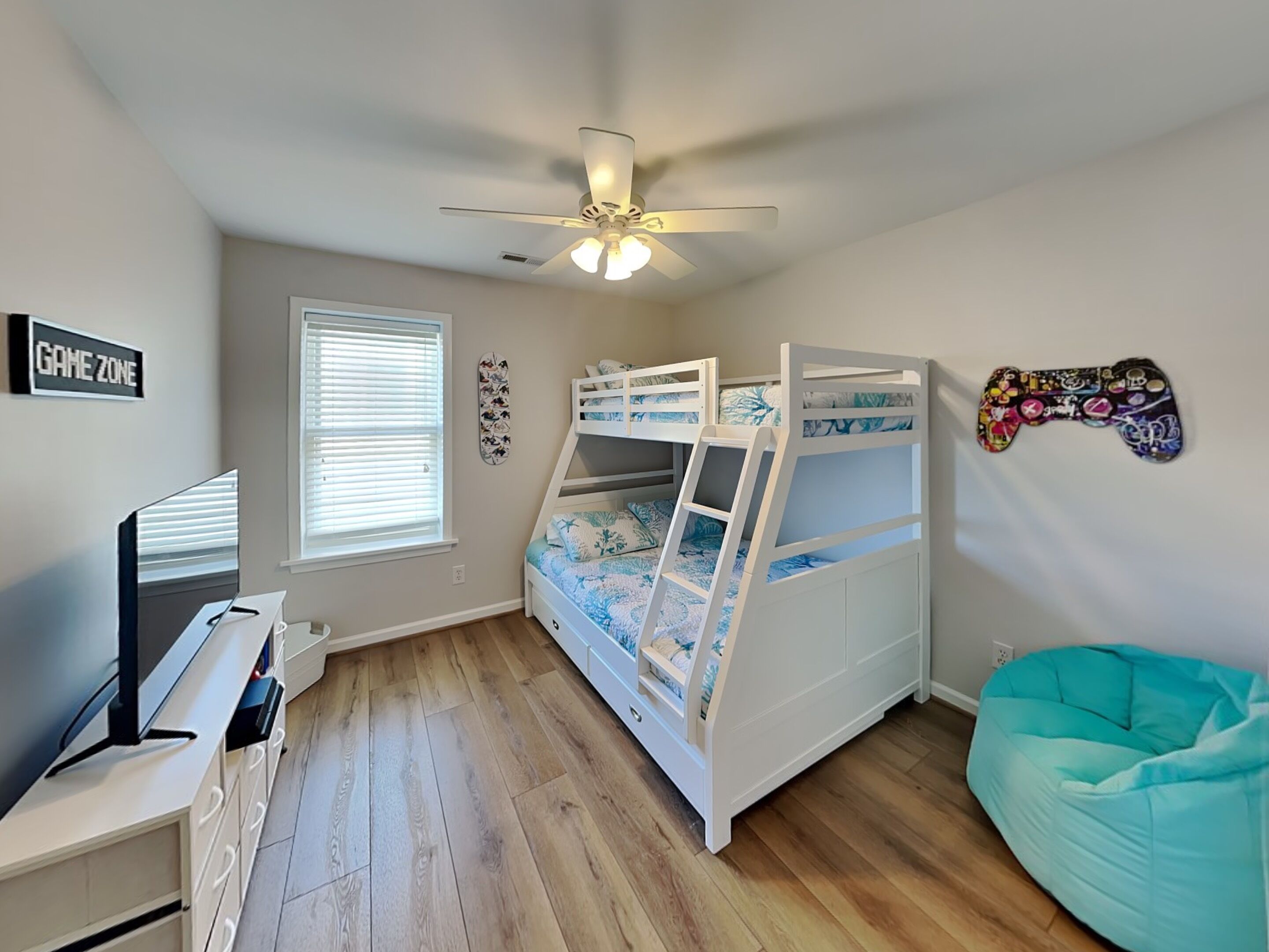 A room with bunk beds, a ceiling fan, a TV, a bean bag, and a wall sign.