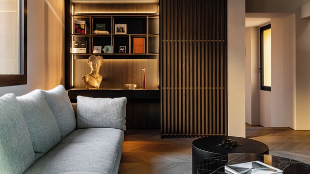 Een moderne woonkamer met een bank, een salontafel, een decoratief beeld en een inbouwkast met diverse spullen.