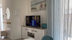 A modern living room with a television, a dining table with a floral plate, a painting of a bicycle, and a window with curtains. - Villa Luigia Garda. "Azure" (Peschiera del Garda)
