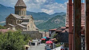 A historic church with a prominent tower, a paved street, and a mountainous backdrop. - River Front Mtskheta (Mtskheta)
