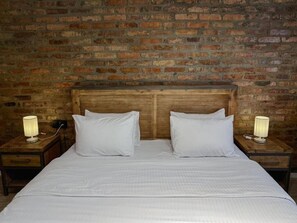 A double bed with a wooden headboard, two bedside tables with lamps, and a brick wall background.