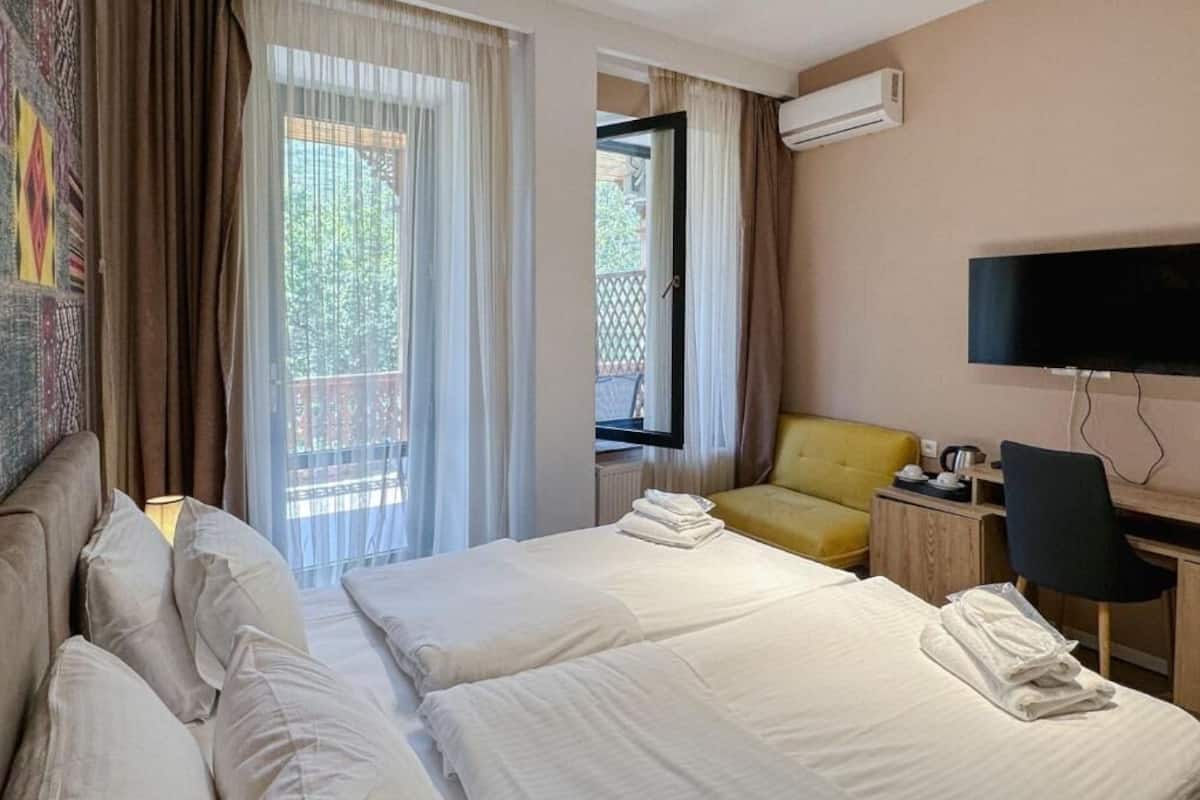 Et hotelværelse med to senge, et skrivebord, en stol, et fjernsyn og en balkon med gardiner.
