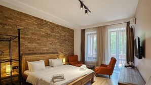 A hotel room with a wooden bed, two chairs, a small table, a TV, and a brick wall. - River Front Mtskheta (Mtskheta)