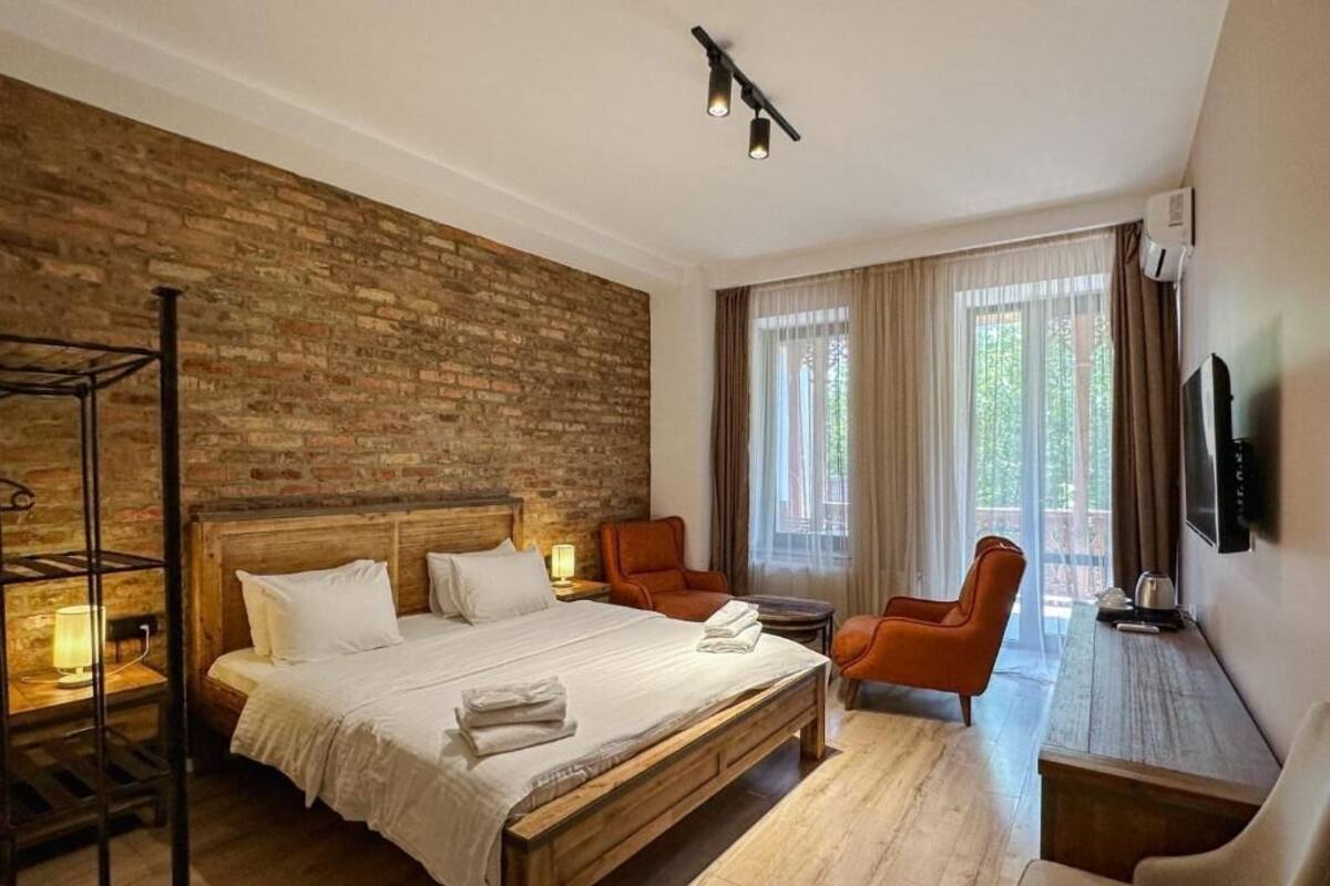 Et hotelværelse med en træseng, to stole, et lille bord, et fjernsyn og en murstensvæg.