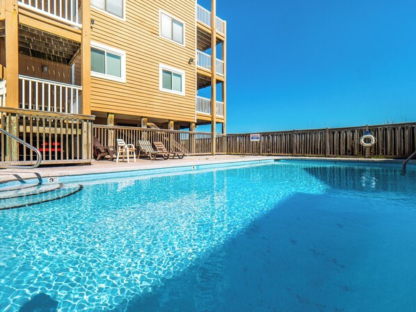 A swimming pool with lounge chairs and a wooden fence. - Sand Pebbles #A3 - Pelican Perch (Carolina Beach)