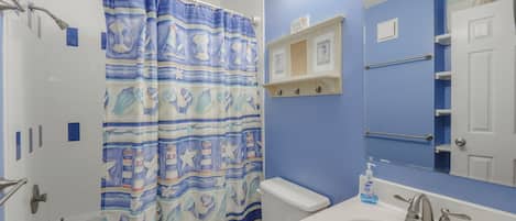 A bathroom with a shower curtain, toilet, sink, and mirror.