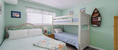 A bedroom with a bunk bed, a single bed, and a nightstand with a lamp.