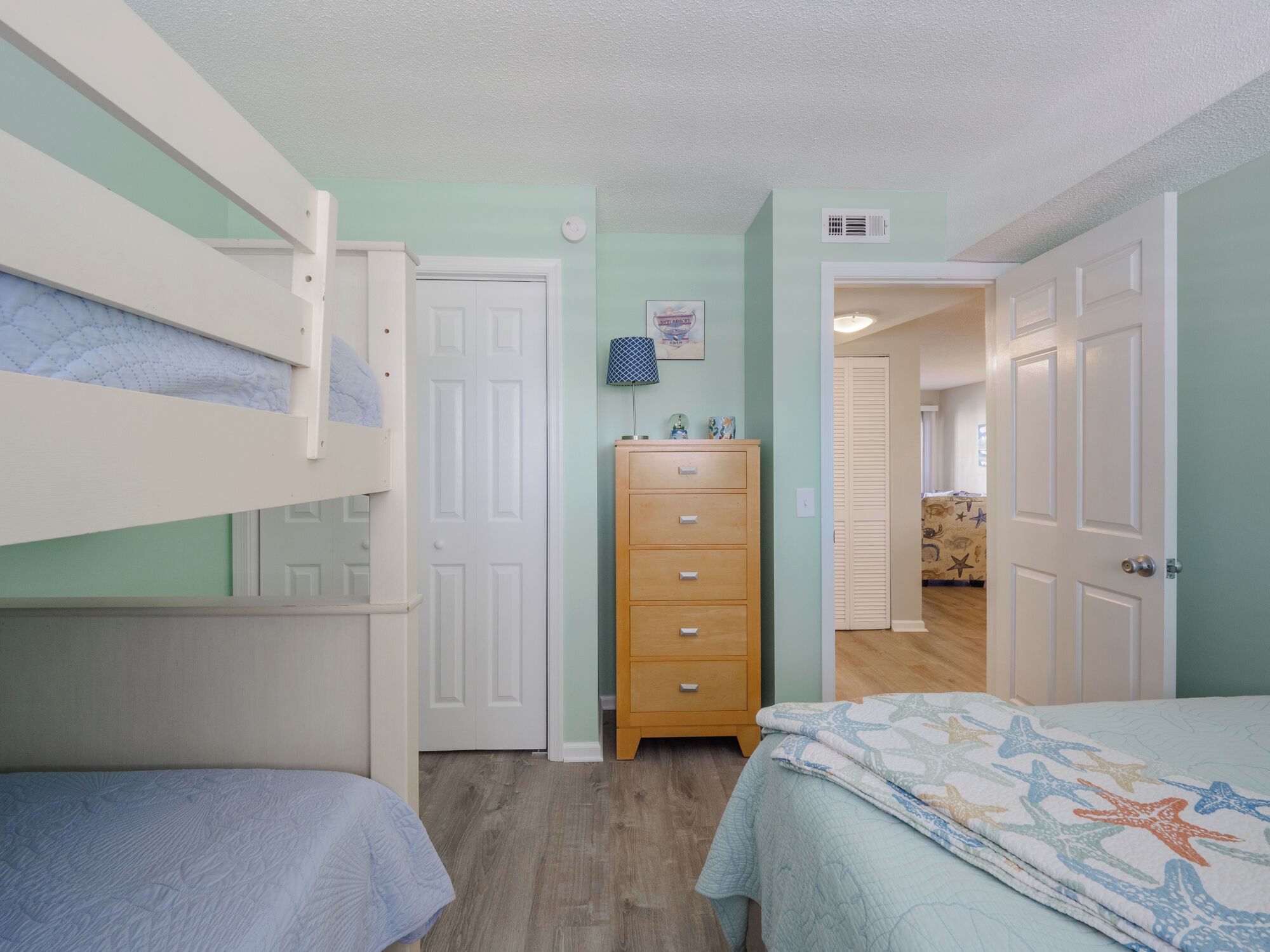 Een slaapkamer met stapelbedden, een dressoir en een deur naar een andere kamer.