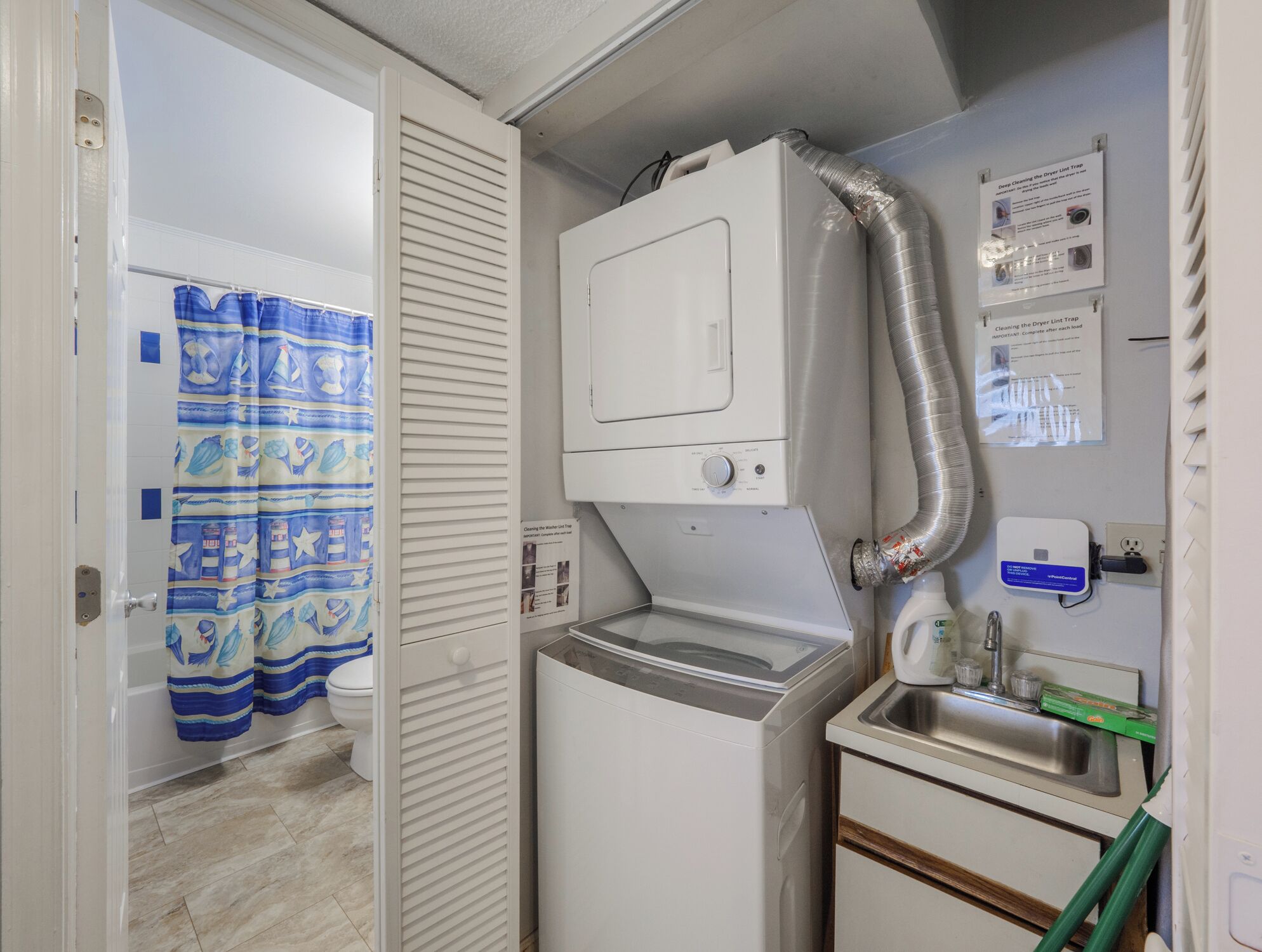 Une cuisine compacte équipée d’un lave-linge et d’un sèche-linge intégrés, d’un petit évier et d’un espace douche agrémenté d’un rideau bleu.