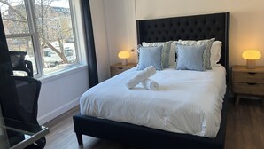Un lit bien fait, avec du linge de lit blanc, une tête de lit capitonnée et deux lampes de chevet.