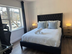 A neatly made bed with white linens, a tufted headboard, and two bedside lamps. - Passion, 2 Queen-size bed, Air-conditioned, Balcony, Free parking (Lévis)