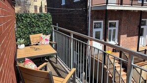 Un balcon avec une table en bois, des chaises et un pot de fleurs.