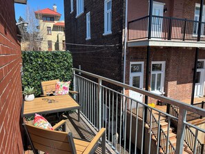 A balcony with a wooden table, chairs, and a potted plant. - Passion, 2 Queen-size bed, Air-conditioned, Balcony, Free parking (Lévis)