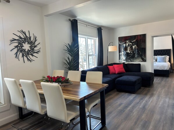 A modern living room with a dining area, a sofa, a bed, and a large window. - Passion, 2 Queen-size bed, Air-conditioned, Balcony, Free parking (Lévis)