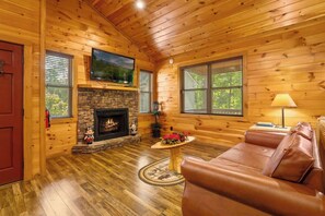 Ein rustikales Blockhaus-Interieur mit Kamin, Ledersofa und einem darüber montierten Fernseher.