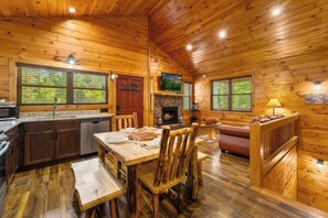 Ein Holzblockhaus-Interieur mit Essbereich, Küche, Kamin und Fernseher.