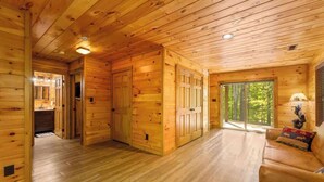 Interior d'una cabana de fusta amb terra de fusta, un sofà i una porta que dona a un balcó.