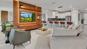Uma sala de estar moderna com televisão de tela plana, um sofá, uma mesa de centro e uma área de cozinha com banquetas.