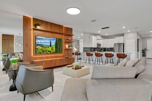 Un salon moderne doté d’un téléviseur à écran plat, d’un canapé, d’une table basse et d’un coin cuisine avec des tabourets de bar.