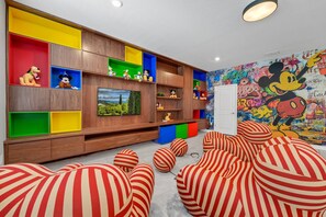 Una sala de estar moderna con televisor, estantes coloridos y un mural de Mickey Mouse.