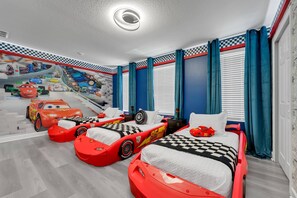 Un dormitorio infantil con camas con forma de coche de carreras, un mural en la pared y cortinas a cuadros.