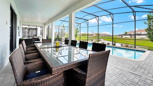 Área externa coberta com mesa de vidro e cadeiras de vime, piscina e vista para um campo de golfe.