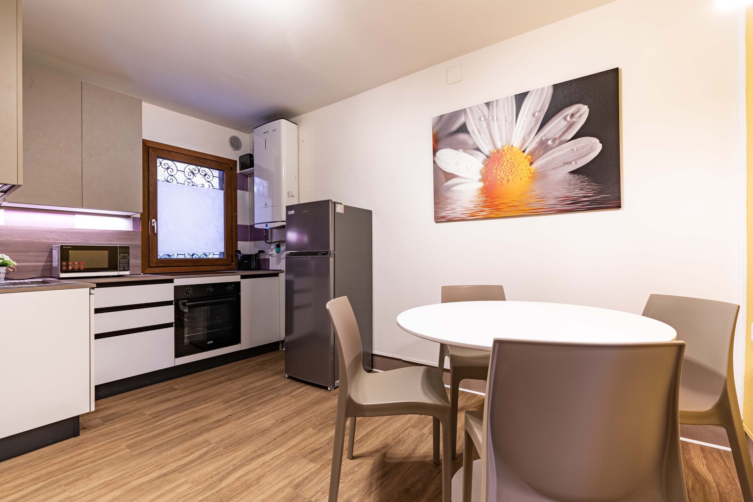 A modern kitchen with a microwave, oven, refrigerator, and a dining area with a round table and chairs.