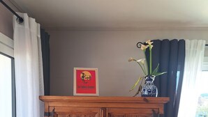 Ett träskåp med en inramad affisch, en vas med blommor och ett fönster med gardiner.