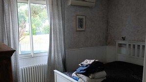 Ett sovrum med en enkelsäng, ett element, ett fönster med gardiner och en tavla på väggen.