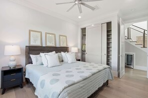 Ein Schlafzimmer mit einem Bett, Nachttischen, einem Deckenventilator, gerahmten Kunstwerken, einem Kleiderschrank und einer Treppe.