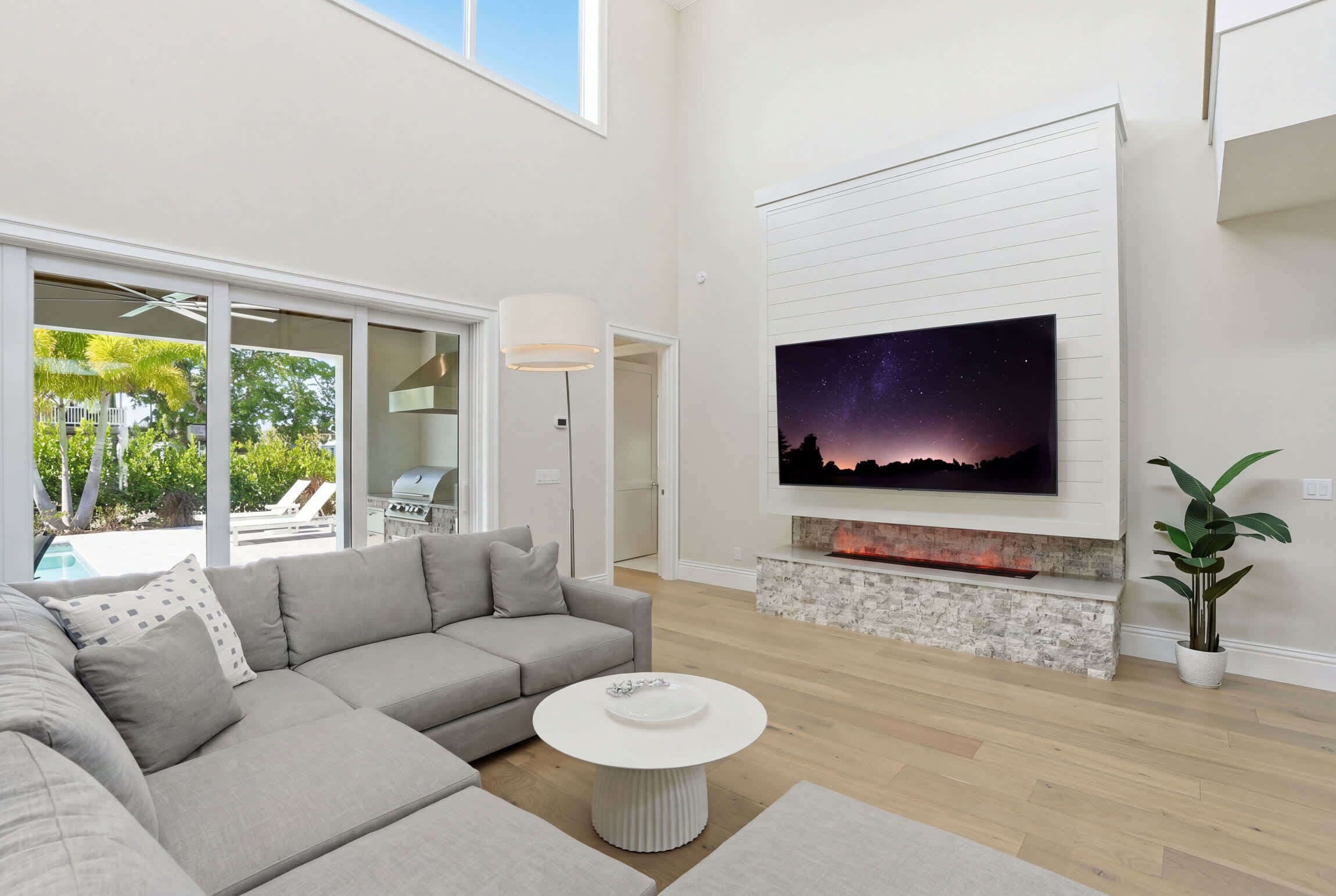 Ein modernes Wohnzimmer mit einem Ecksofa, einem runden Couchtisch, einem Kamin und einem großen Fernseher, der an der Wand befestigt ist.
