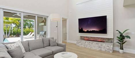 Ein modernes Wohnzimmer mit einem Ecksofa, einem runden Couchtisch, einem Kamin und einem großen Fernseher, der an der Wand befestigt ist.