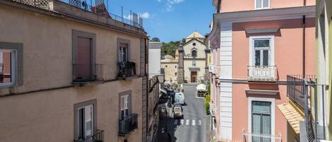 Una calle estrecha bordeada por edificios con balcones, una iglesia al fondo y un cielo azul despejado.