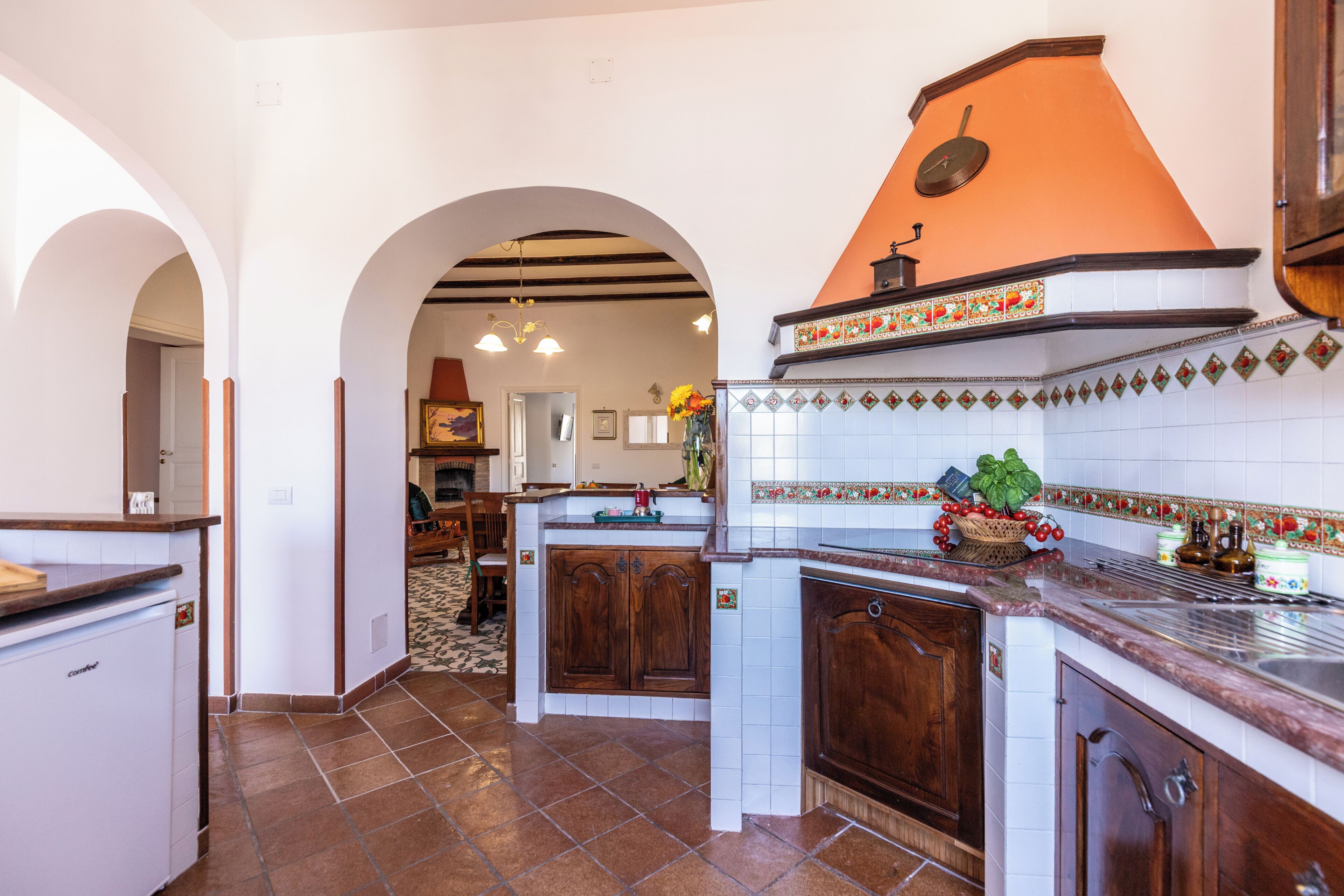 A kitchen with a central island, wooden cabinets, a tiled backsplash, and an archway leading to another room.