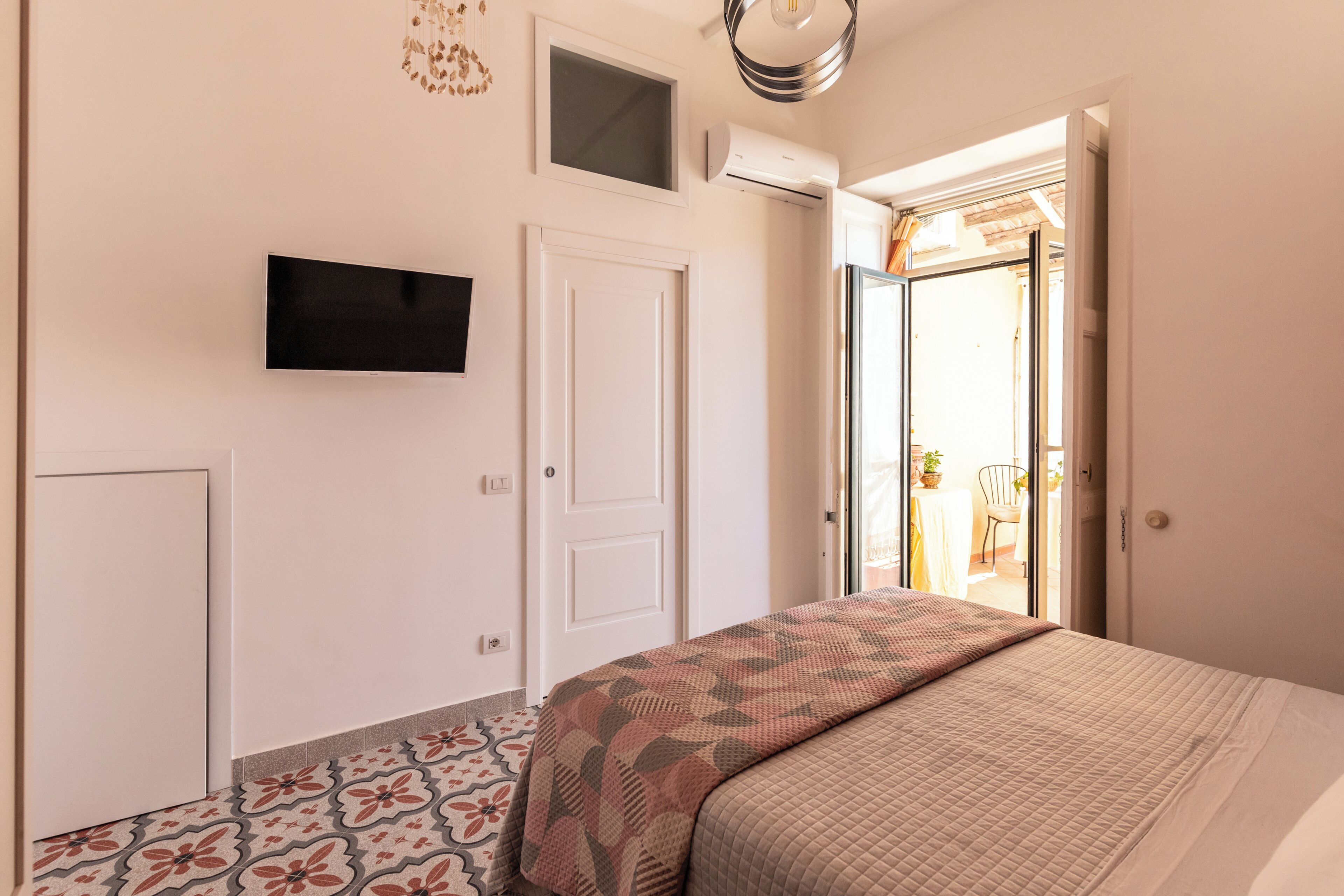 A bedroom with a bed, a TV mounted on the wall, a door, and a window.