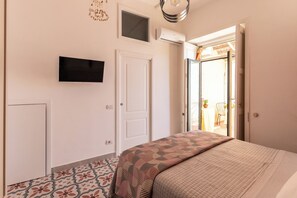 A bedroom with a bed, a TV mounted on the wall, a door, and a window. - La Palommella (Massa Lubrense)