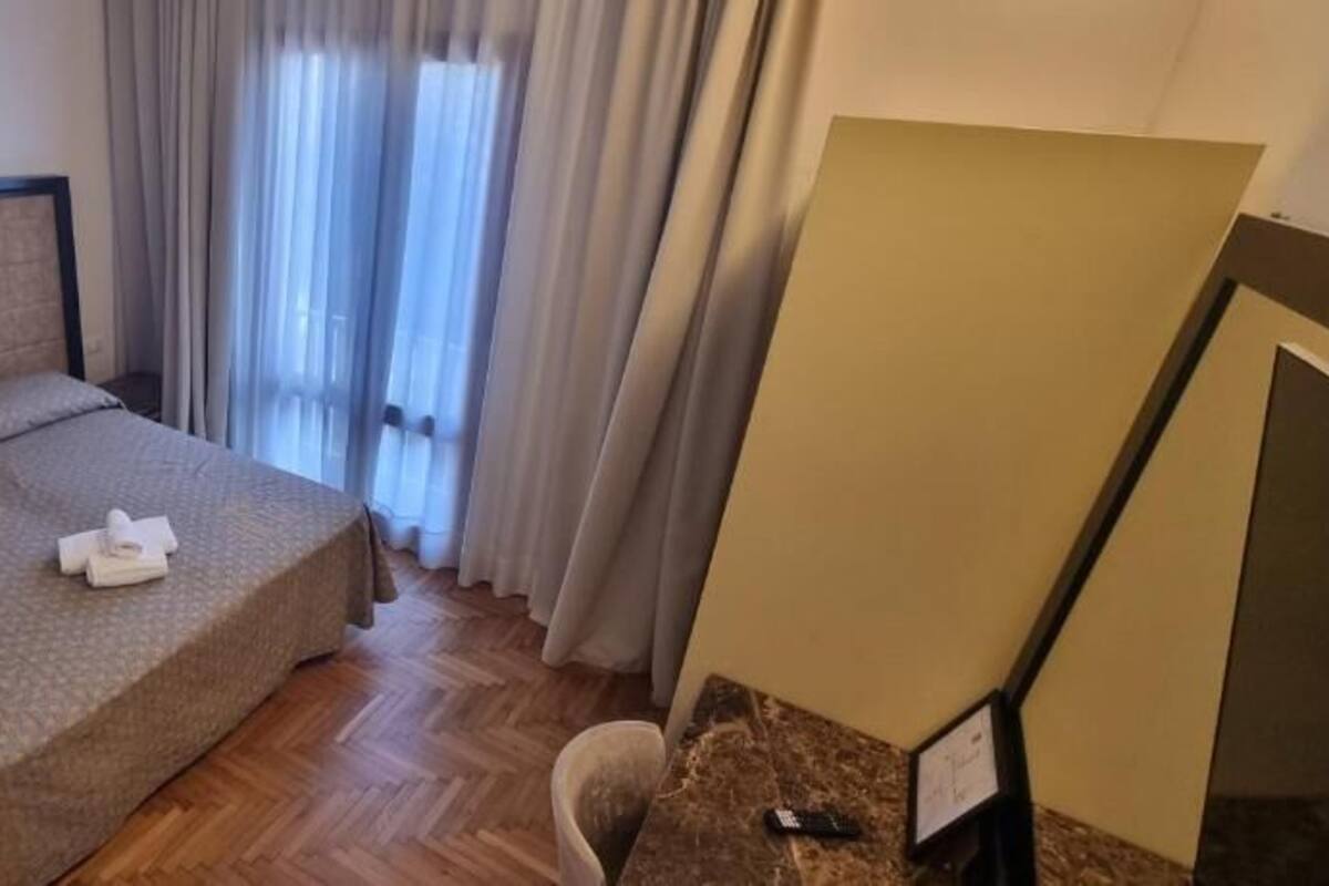 Una camera d'albergo con un letto, una scrivania, una sedia e una finestra con tende.