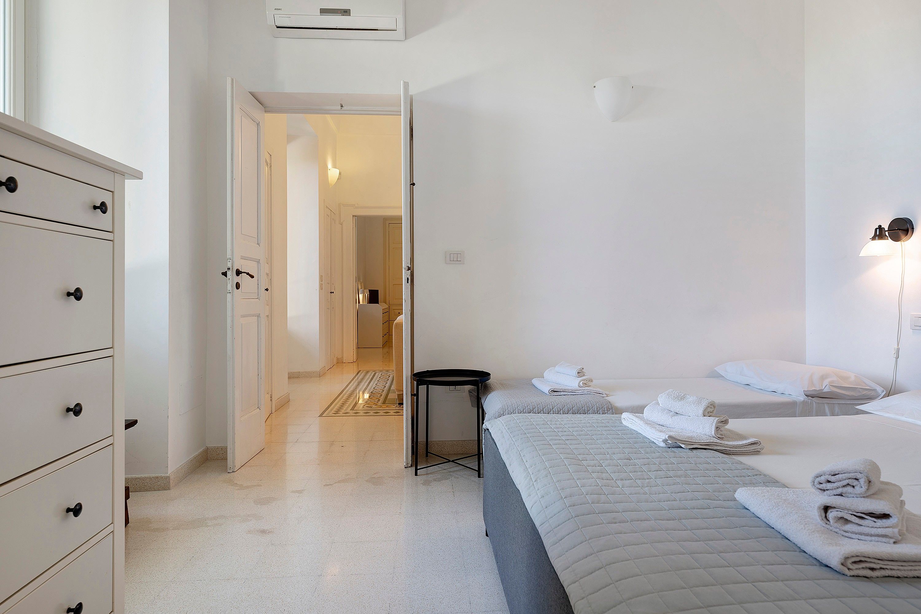 Une chambre d’hôtel avec un lit, une table de chevet, une armoire et une salle de bain visible à travers une porte ouverte.