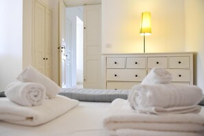 Une chambre d’hôtel avec un lit, une lampe de chevet, une commode blanche et une porte donnant sur une autre pièce.
