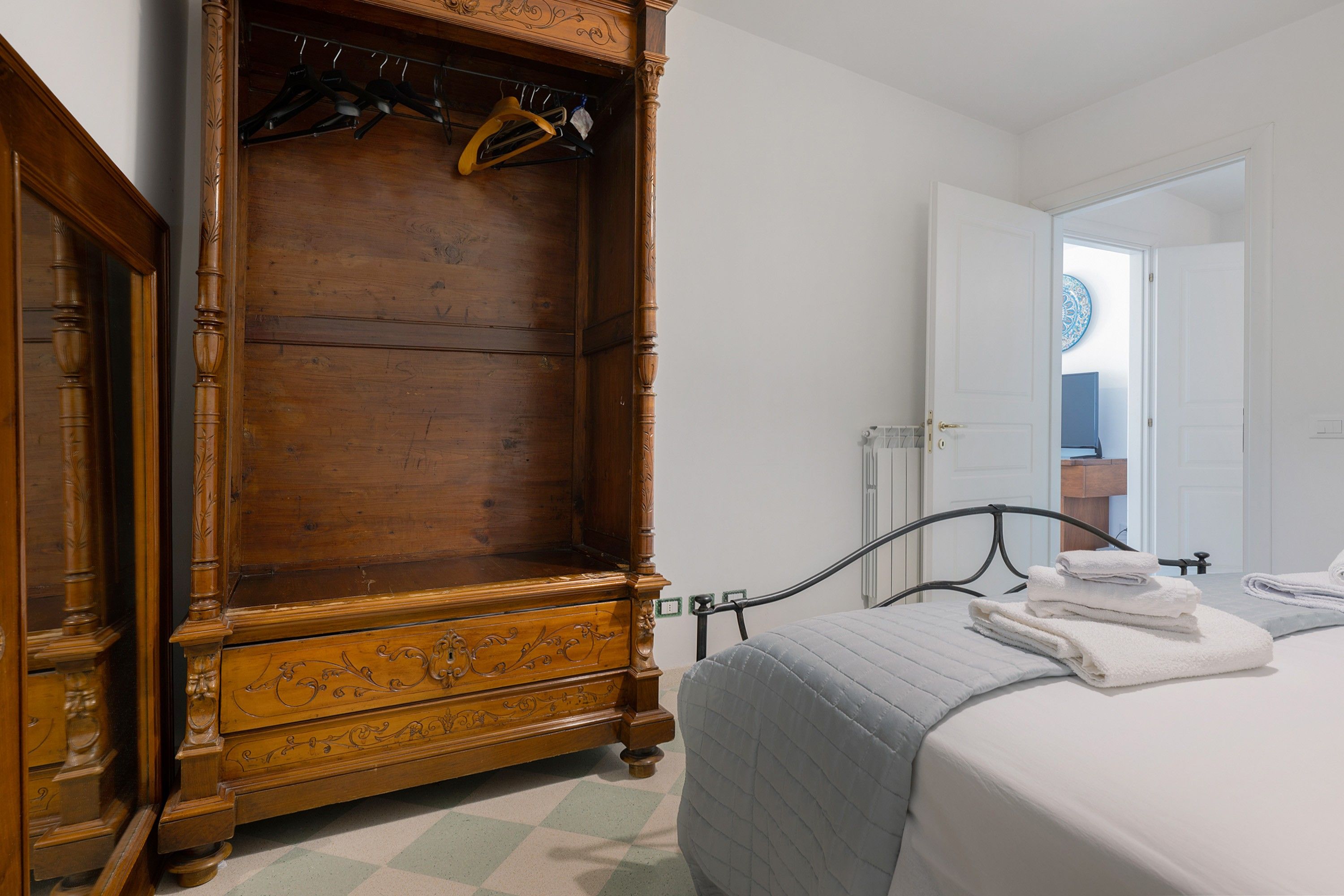 Quarto com armário de madeira, cama com colcha cinza e banheiro visível por uma porta aberta.