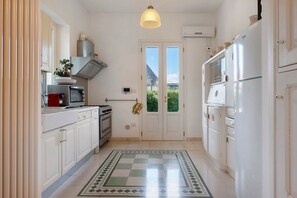 A compact kitchen with white cabinets, a stove, a microwave, and a refrigerator. - Villa 'Luciana' with Private Terrace, Wi-Fi, and Air Conditioning (Martina Franca)