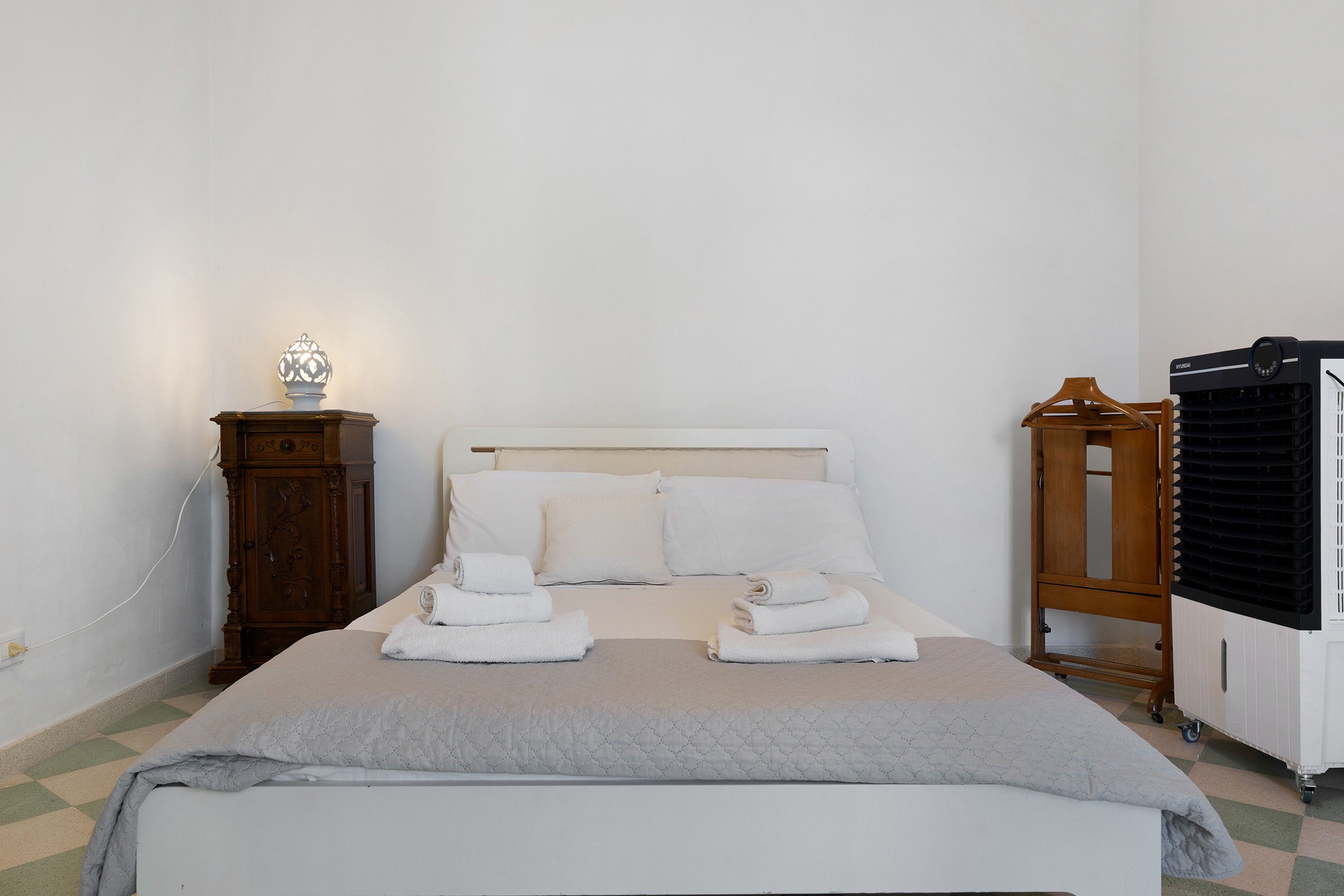 A neatly made bed with a white headboard, a bedside table with a lamp, and a wooden cabinet.