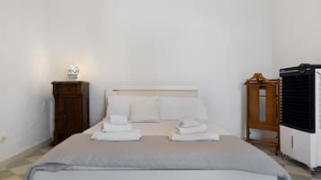 A neatly made bed with a white headboard, a bedside table with a lamp, and a wooden cabinet.