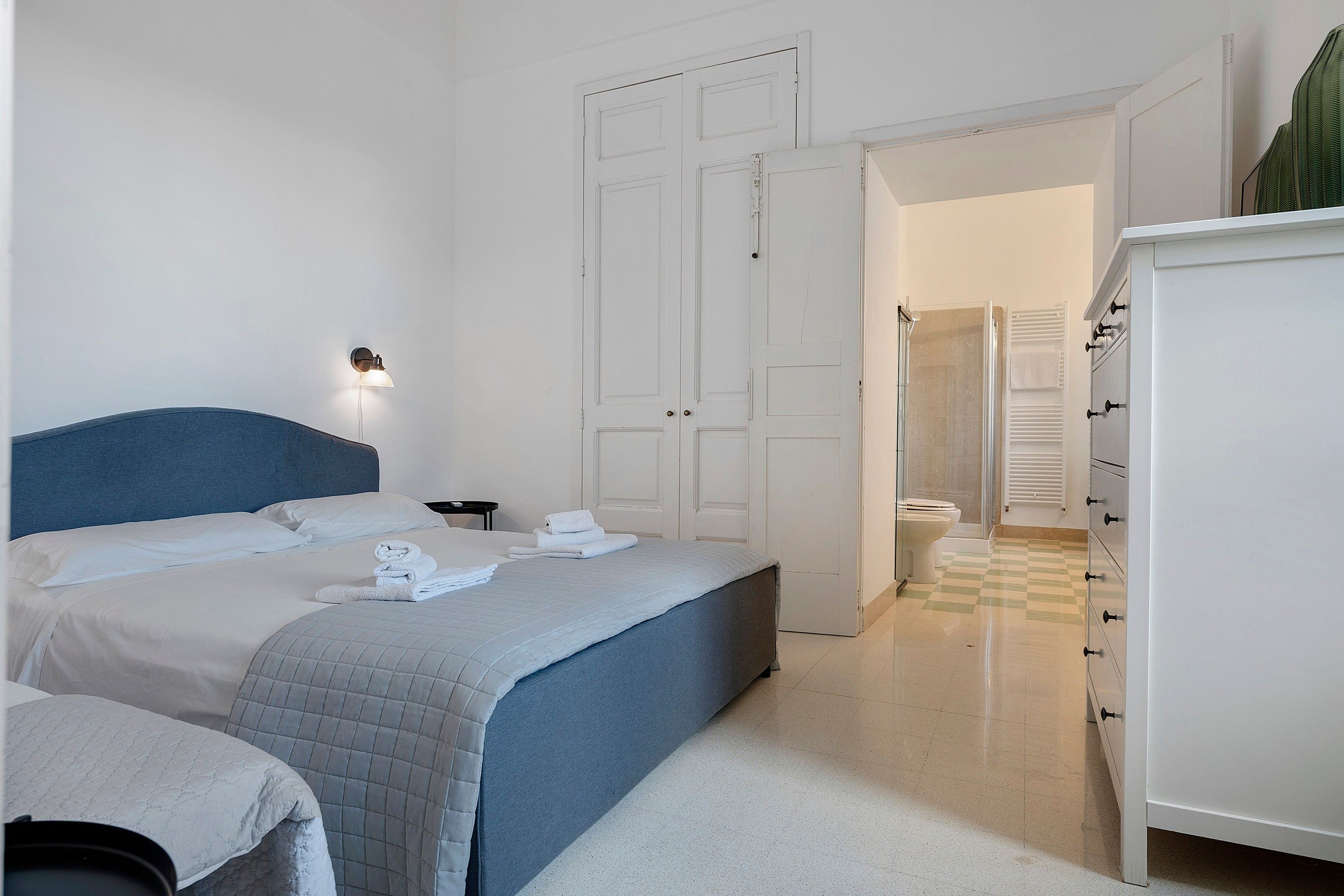 A hotel room with a bed, a bedside table, a wardrobe, and a shower area.