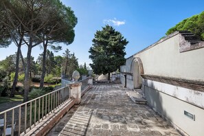 A pathway leading to a building with a stone-tiled floor and a metal railing on one side.